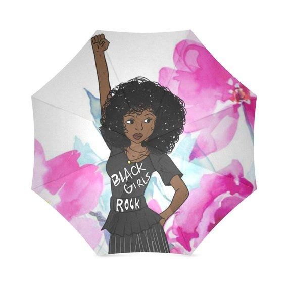A waterproof umbrella with a print of a black girl with an afro and the text 'Black Girls Rock' on a pink and blue floral background.